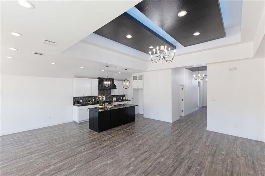 Kitchen featuring an island with sink, open floor plan, hanging light fixtures, a tray ceiling, and white cabinetry