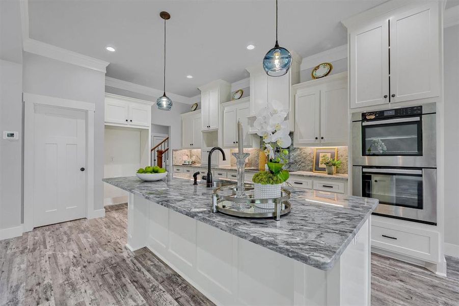 Kitchen with pendant lighting, light stone counters, white cabinets, backsplash, and double oven