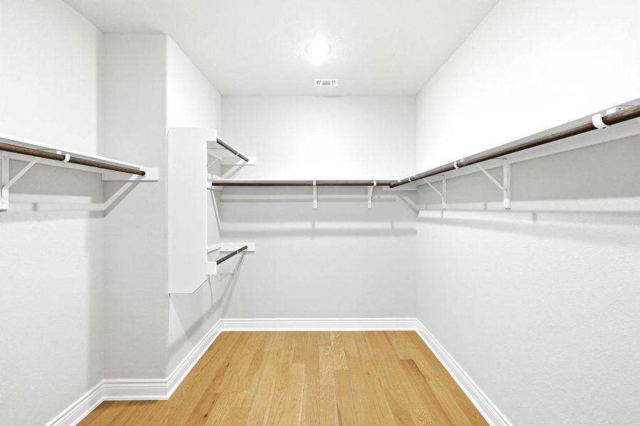 Expansive walk-in closet featuring light wood-finish flooring, white baseboards, white walls, and built-in white shelving with hanging rods