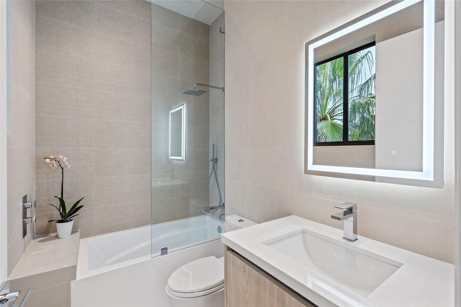 Sleek modern bathroom with glass-enclosed shower/tub, vanity, and illuminated LED mirror. Sleek modern bathroom with glass-enclosed shower/tub, vanity, and illuminated LED mirror.