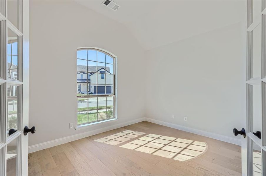 Spare room featuring light hardwood / wood-style floors, lofted ceiling, and french doors