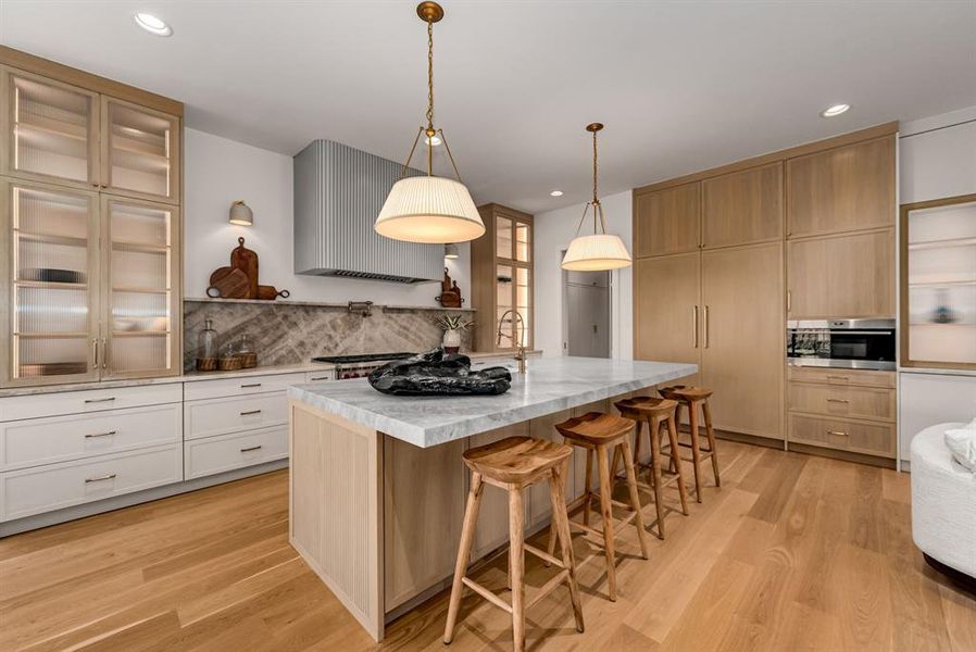 Kitchen with light brown cabinets, exhaust hood, a breakfast bar area, light wood-type flooring, and recessed lighting Kitchen with light brown cabinets, exhaust hood, a breakfast bar area, light wood-type flooring, and recessed lighting