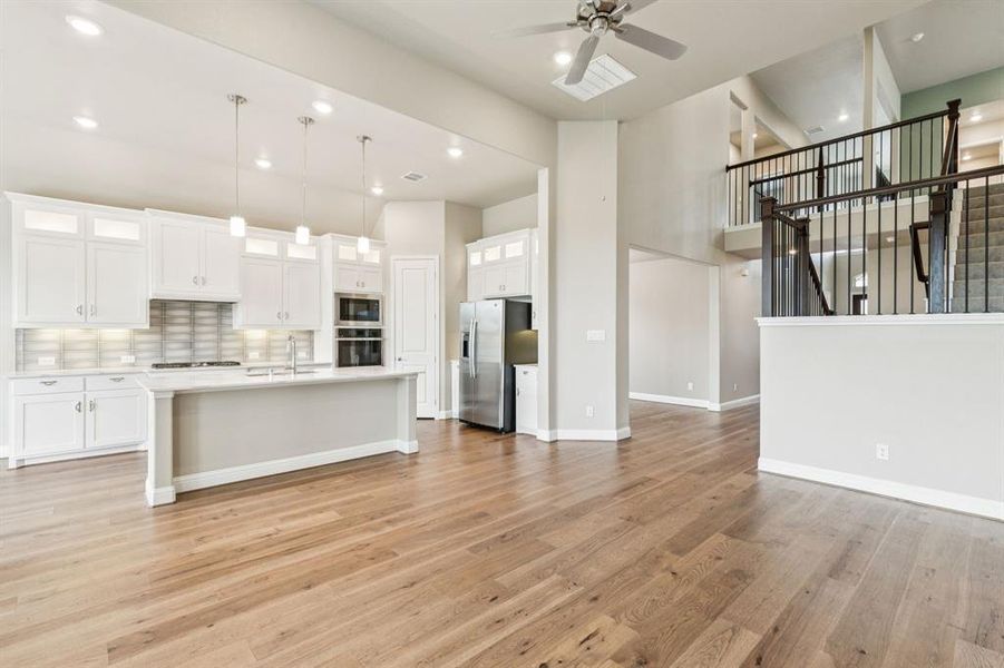 Kitchen with stainless steel appliances, open floor plan, ceiling fan, light wood-style flooring, and light countertops