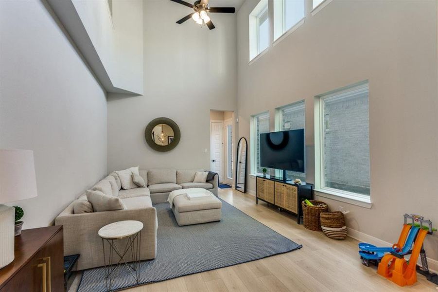 Living room with ceiling fan, a high ceiling, baseboards, and wood finished floors