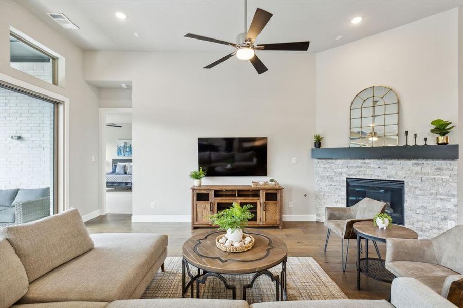 Living room featuring a fireplace, hardwood / wood-style floors, a high ceiling, and ceiling fan