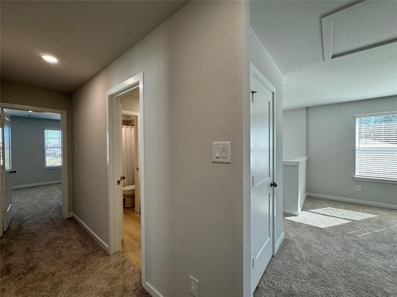 Bright, carpeted upstairs hallway leading to three bedrooms and a full bathroom, featuring white walls, doors, and ample natural light. Bright, carpeted upstairs hallway leading to three bedrooms and a full bathroom, featuring white walls, doors, and ample natural light.