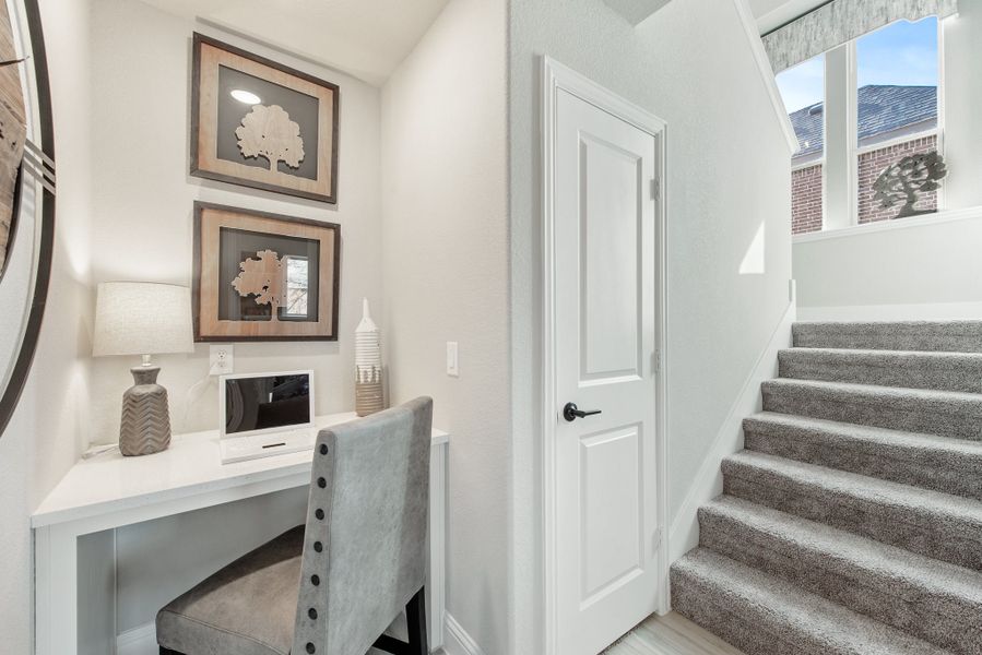Built-in desk nook with white workspace and gray chair beside carpeted staircase