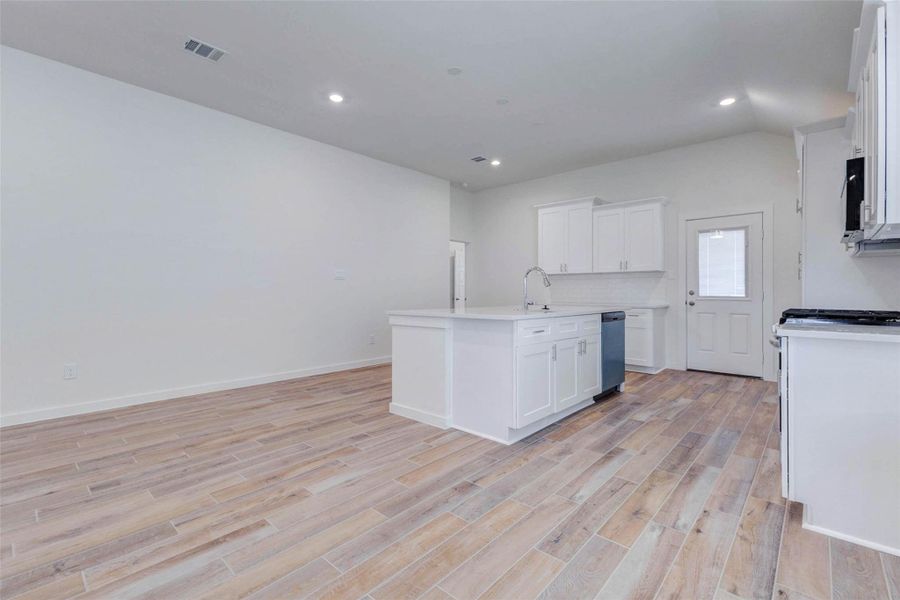 Bright kitchen and dining area featuring wood-look tile flooring, white shaker cabinetry, quartz-style countertops, center island, stainless dishwasher, recessed lighting, and open space for dining. The kitchen flows seamlessly into the main living area for easy entertaining.