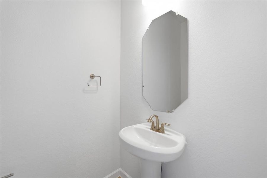 Pedestal sink with brushed brass faucet and an octagonal frameless mirror Pedestal sink with brushed brass faucet and an octagonal frameless mirror