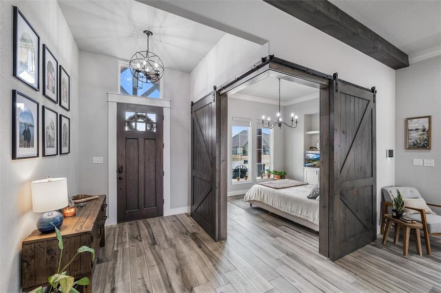 Foyer with a notable chandelier, ornamental molding, a barn door, beamed ceiling, and light wood-type flooring