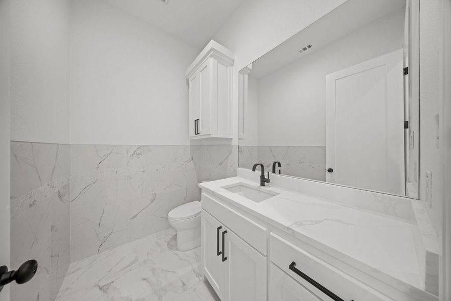 Bathroom featuring tile walls, vanity, light marble finish floors, and wainscoting