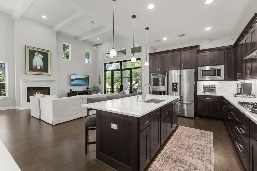 An open concept kitchen and living area feature a spacious island, rich cabinetry, and a cozy fireplace, all bathed in natural light.