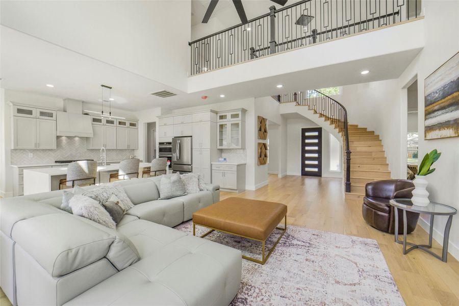 This modern open-concept living space features a spacious kitchen with an island, elegant cabinetry, and stainless steel appliances. The living area boasts a cozy sectional, a stylish ottoman, and abundant natural light. A spiral staircase leads to the upper level, complemented by hardwood floors and contemporary decor.