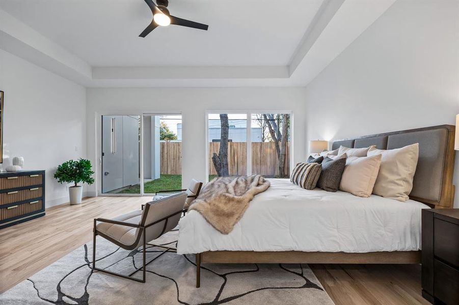 Bedroom with a water view, light hardwood / wood-style flooring, a tray ceiling, ceiling fan, and access to exterior