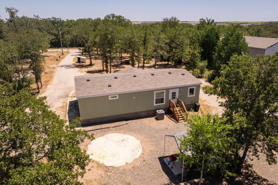 Mature trees surround this private acreage featuring a functional single-story layout with a shingled roof.