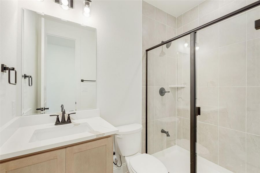Bathroom with single vanity, white countertop, and glass-enclosed tiled shower with dark hardware fixtures.