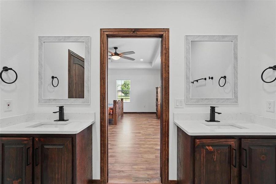 Bathroom featuring two vanities, a tray ceiling, wood finished floors, a ceiling fan, and recessed lighting Bathroom featuring two vanities, a tray ceiling, wood finished floors, a ceiling fan, and recessed lighting