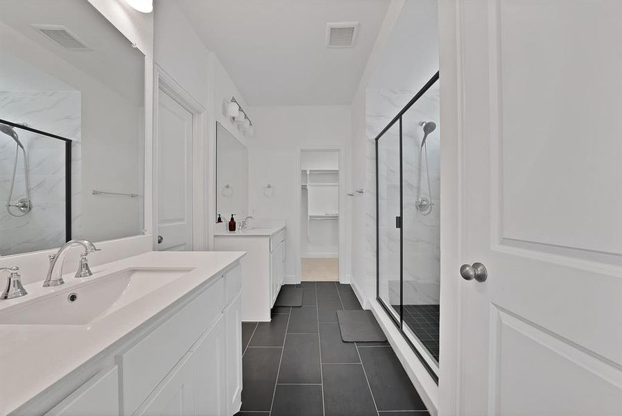 Spacious bathroom featuring dual white vanities with integrated sinks, brushed nickel fixtures, a large frameless mirror, and modern tile flooring