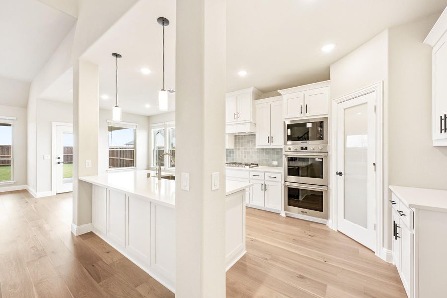 Kitchen with white cabinets, center island, stainless steel double ovens, and light hardwood floors