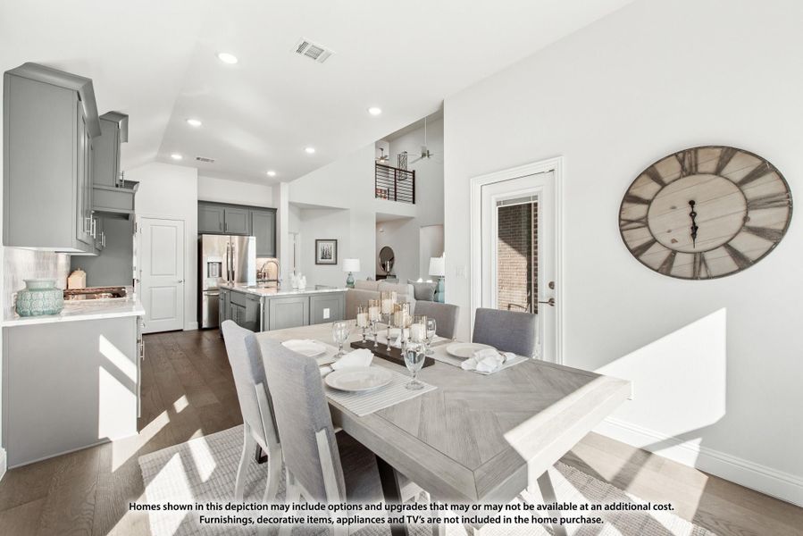 Open-concept dining area with set table flowing into kitchen with gray cabinets and stainless appliances Open-concept dining area with set table flowing into kitchen with gray cabinets and stainless appliances