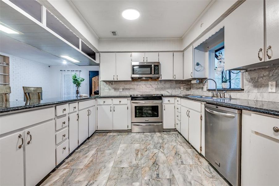 Kitchen featuring stainless steel appliances, backsplash, a sink, and white cabinetry
