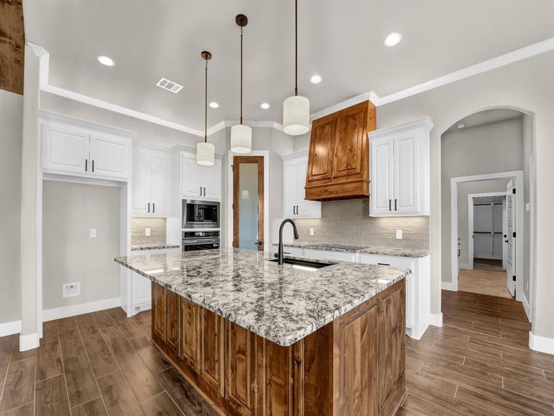 Kitchen with brown cabinetry, wood finish floors, light stone counters, decorative backsplash, and recessed lighting