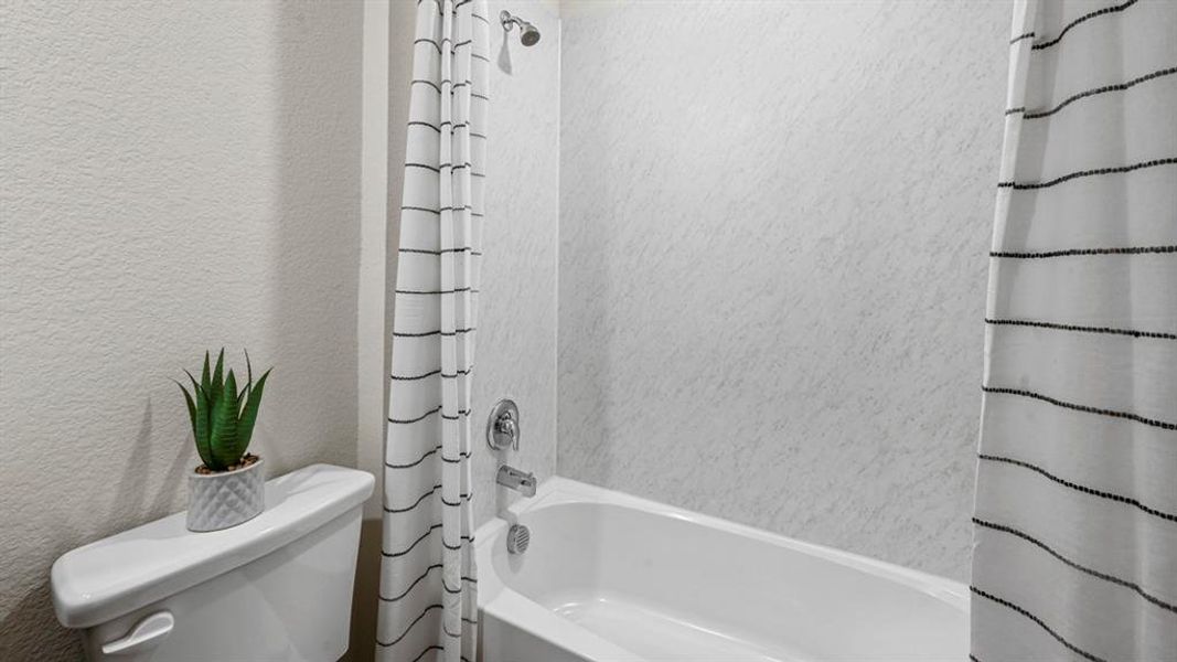 Bathroom featuring shower / bath combo with shower curtain and a textured wall Bathroom featuring shower / bath combo with shower curtain and a textured wall