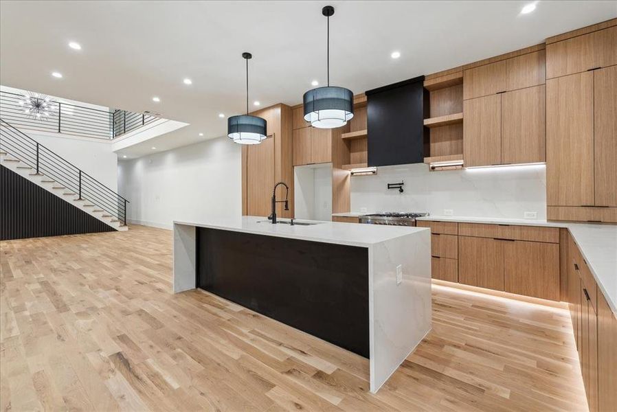 Kitchen with pendant lighting, sink, a kitchen island with sink, light hardwood / wood-style flooring, and exhaust hood