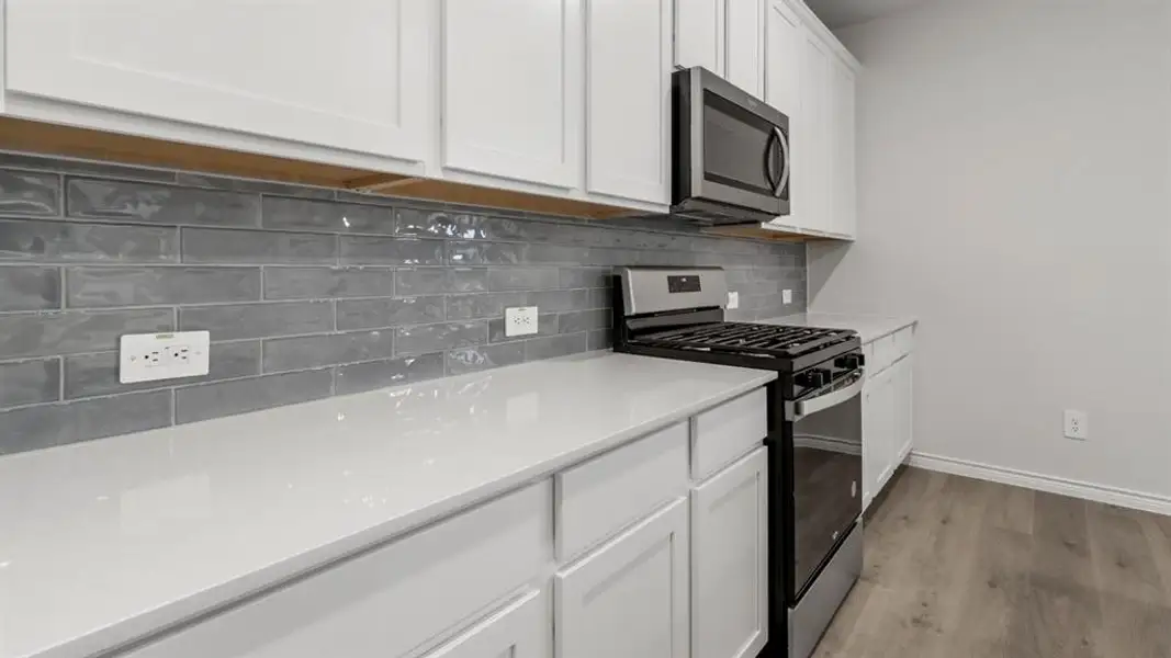 Kitchen with stainless steel appliances, white cabinets, tasteful backsplash, light wood finished floors, and light stone countertops Kitchen with stainless steel appliances, white cabinets, tasteful backsplash, light wood finished floors, and light stone countertops