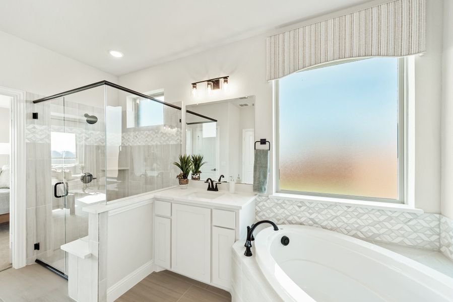 Master bathroom with glass walk-in shower, soaking tub, white vanity, and large frosted window