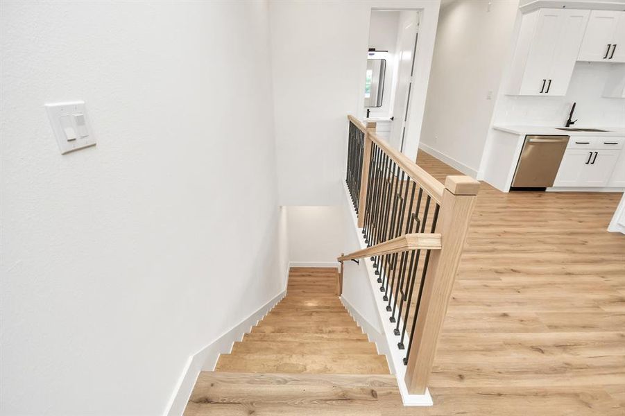 This interior staircase features a modern, open design with warm wood flooring and a sleek black metal railing, offering a stylish yet functional transition between levels. The stairway connects seamlessly to the bright and spacious kitchen area, enhancing the home’s open-concept layout.