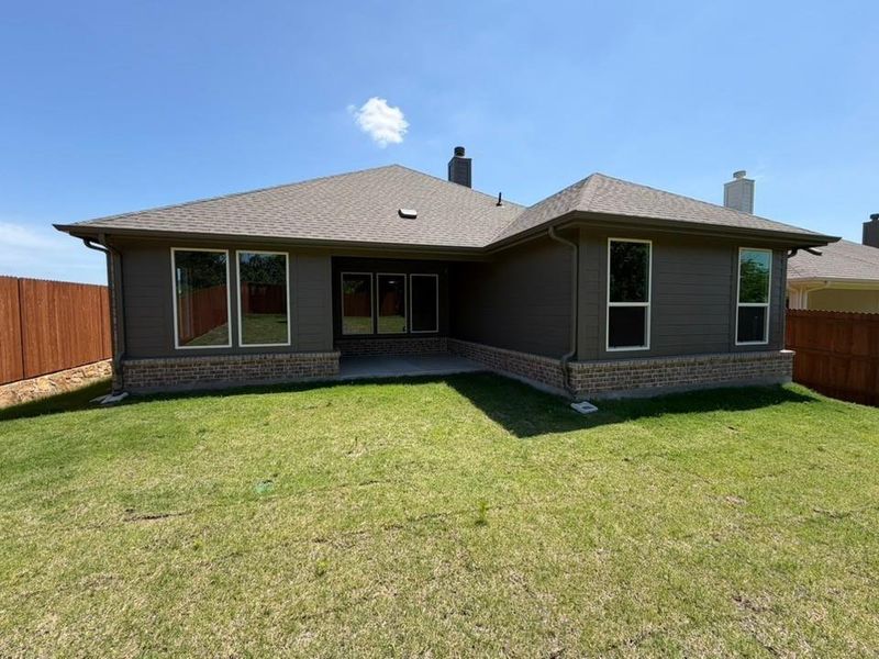 Rear exterior featuring dark gray siding, a brick base, multiple windows, a covered patio, and a fenced backyard