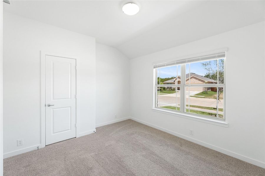 Empty bedroom with white walls, beige carpet, a closet door, and a large window overlooking a neighborhood street.