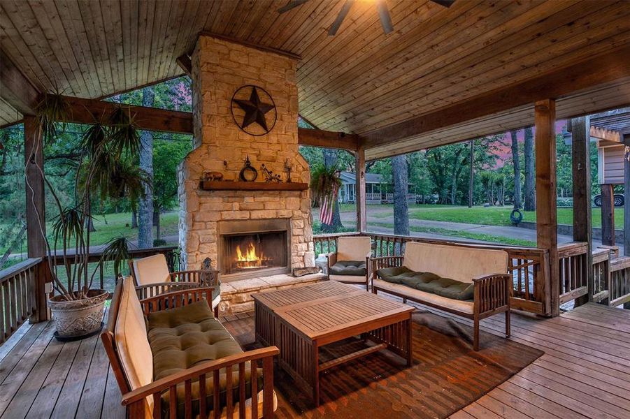 Expansive covered porch featuring a stone-clad fireplace with a wood mantel, exposed wooden beams, and a wood-plank ceiling