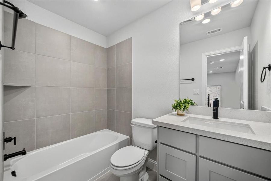 Bathroom featuring a tub/shower combination with large format grey tiling, built-in shower niche, and matte black fixtures