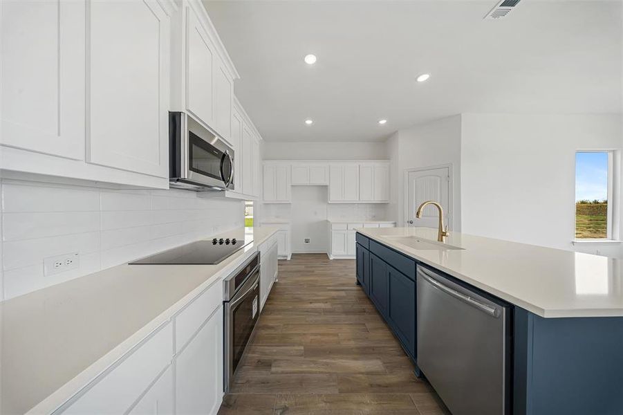 Kitchen with white cabinetry, stainless steel appliances, blue cabinetry, a kitchen island with sink, and dark wood-type flooring Kitchen with white cabinetry, stainless steel appliances, blue cabinetry, a kitchen island with sink, and dark wood-type flooring