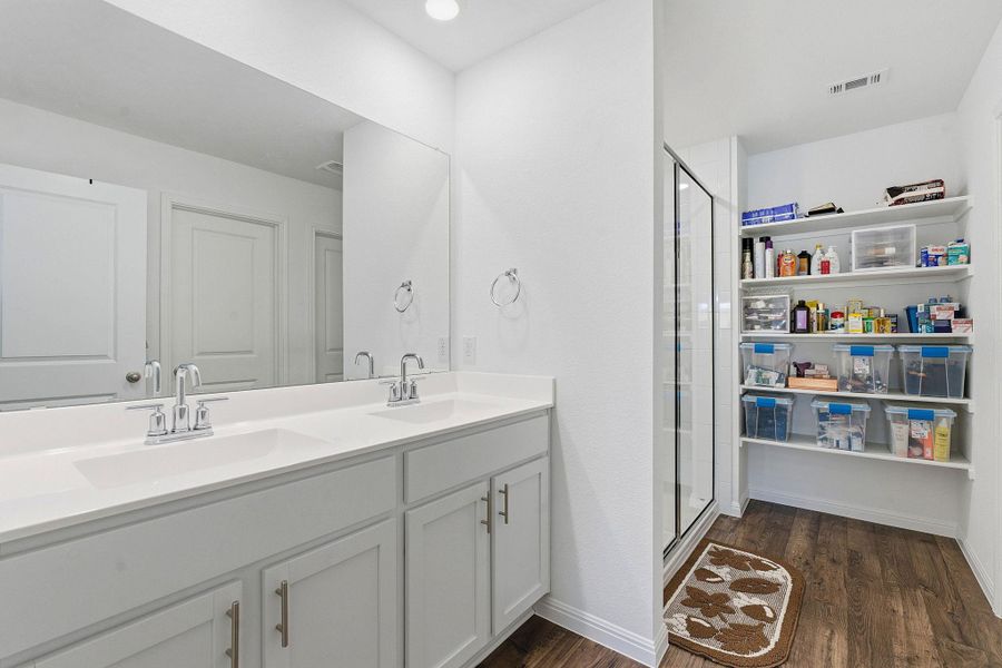 Bathroom with double vanity, a shower stall, and dark wood-type flooring