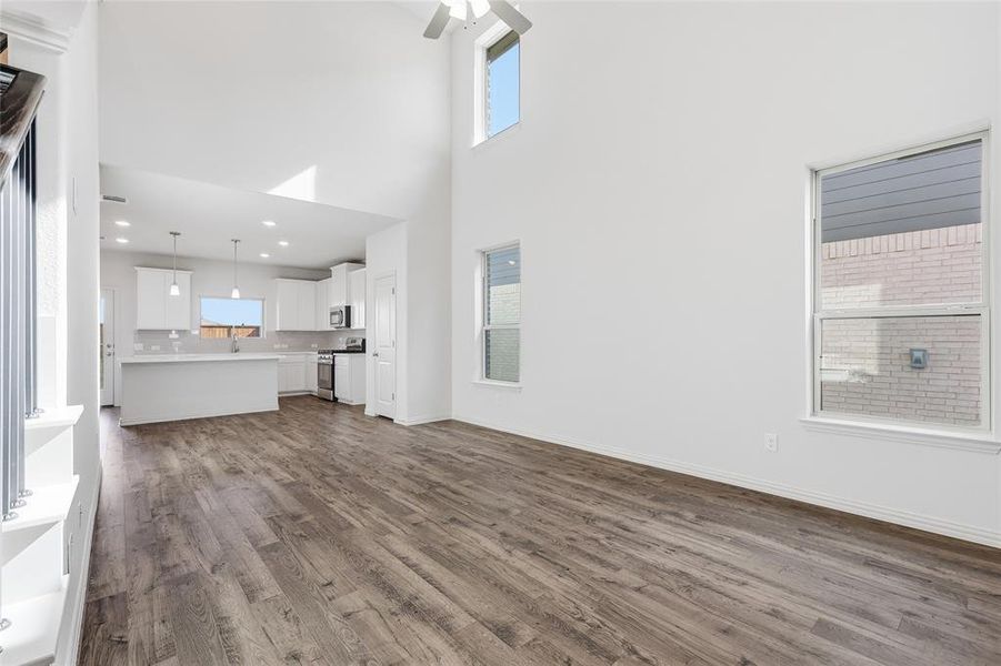 Open-concept living area featuring wood-finish flooring, high ceilings, multiple windows, and a ceiling fan