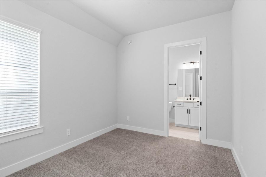 The ideal setup for multi-generational living or extended stays, this bedroom includes its own dedicated en suite bath, ensuring privacy for all. It features sloped ceilings, large window, plush carpet flooring, and neutral-toned walls.