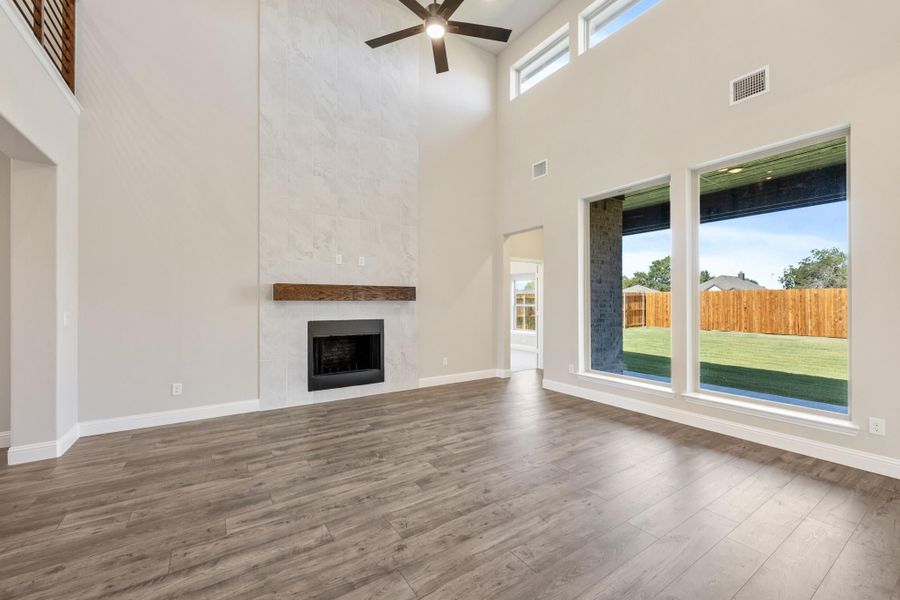 Open living room with high ceilings, tile fireplace, wood mantel, hardwood floors, and large windows overlooking backyard Open living room with high ceilings, tile fireplace, wood mantel, hardwood floors, and large windows overlooking backyard