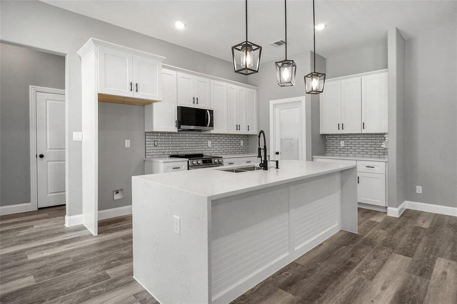 Kitchen with stainless steel appliances, tasteful backsplash, white cabinetry, a center island with sink, and recessed lighting Kitchen with stainless steel appliances, tasteful backsplash, white cabinetry, a center island with sink, and recessed lighting