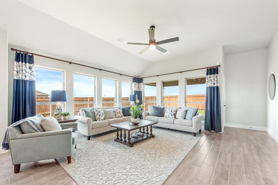 Living room with vaulted ceiling, ceiling fan, multiple windows, and two sofas with blue curtains and wood-look floors