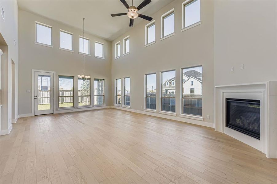 Unfurnished living room with light wood-type flooring, a glass covered fireplace, a chandelier, ceiling fan, and healthy amount of natural light