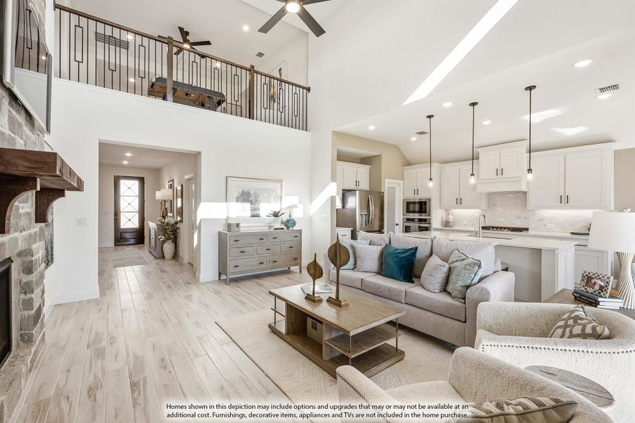 Open-concept living room with two-story ceiling, stone fireplace, and kitchen visible in background Open-concept living room with two-story ceiling, stone fireplace, and kitchen visible in background