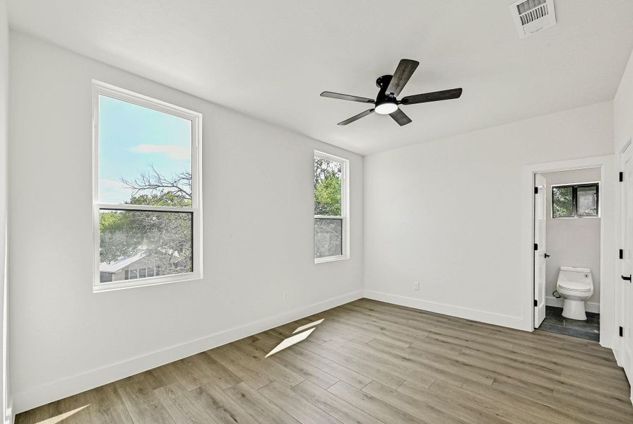 Unfurnished bedroom with light wood-type flooring, multiple windows, a ceiling fan, and ensuite bathroom