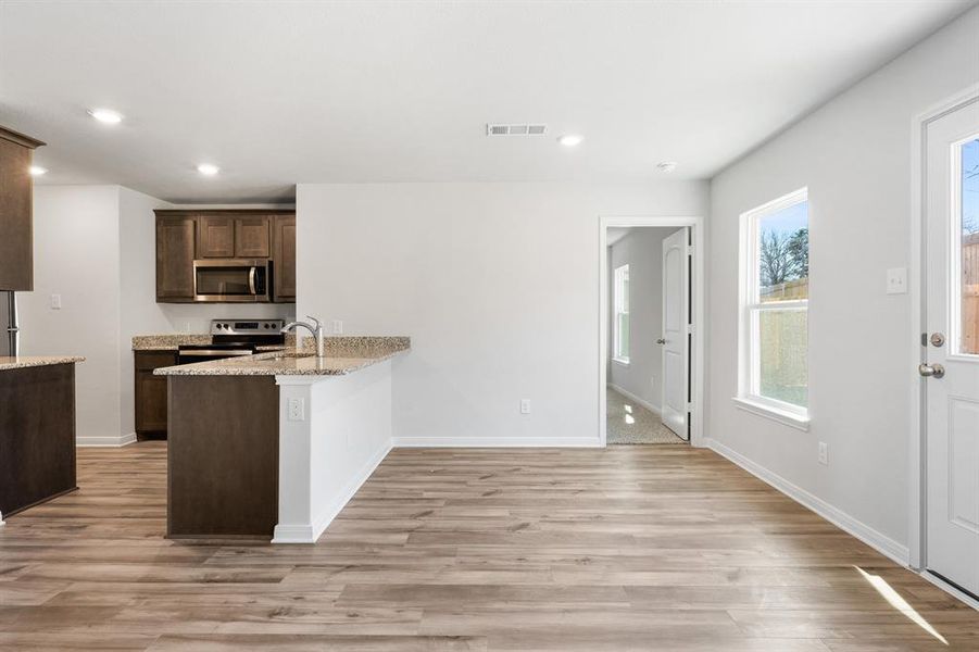 Kitchen featuring appliances with stainless steel finishes, sink, light stone counters, light wood-type flooring, and kitchen peninsula