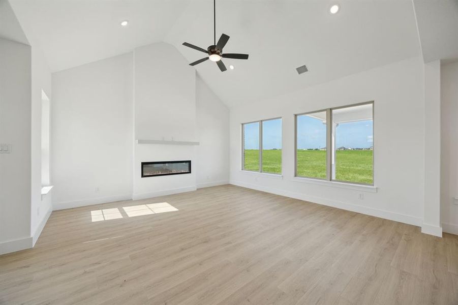 Unfurnished living room with high vaulted ceiling, light wood-style floors, a glass covered fireplace, ceiling fan, and recessed lighting Unfurnished living room with high vaulted ceiling, light wood-style floors, a glass covered fireplace, ceiling fan, and recessed lighting