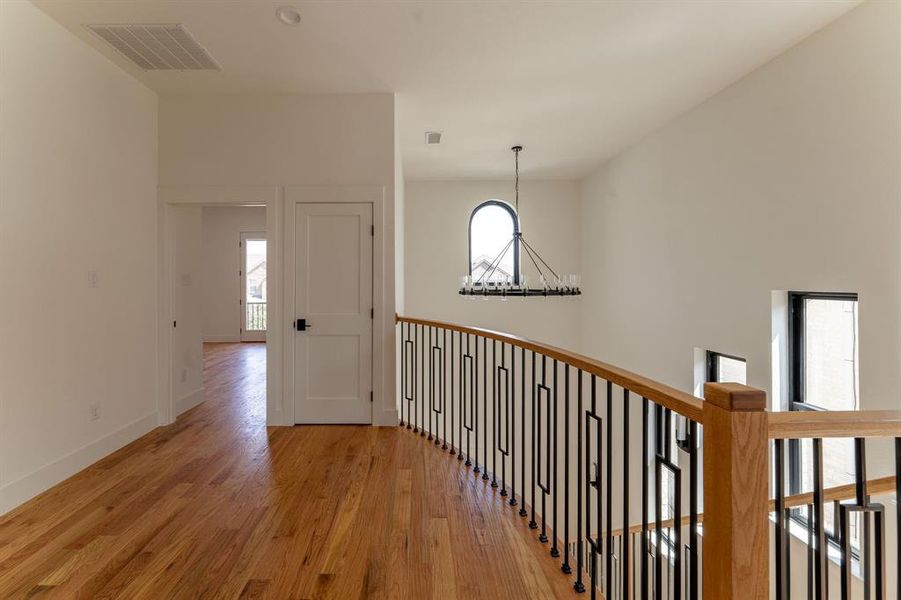 Corridor featuring healthy amount of natural light, light wood finished floors, and a chandelier
