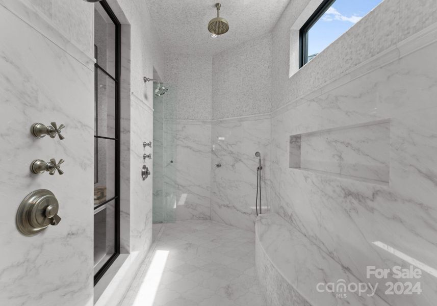 Expansive walk thru shower adorned with marble from the ceiling to the floor. The shower features rain shower heads, body sprayers, and traditional shower heads.