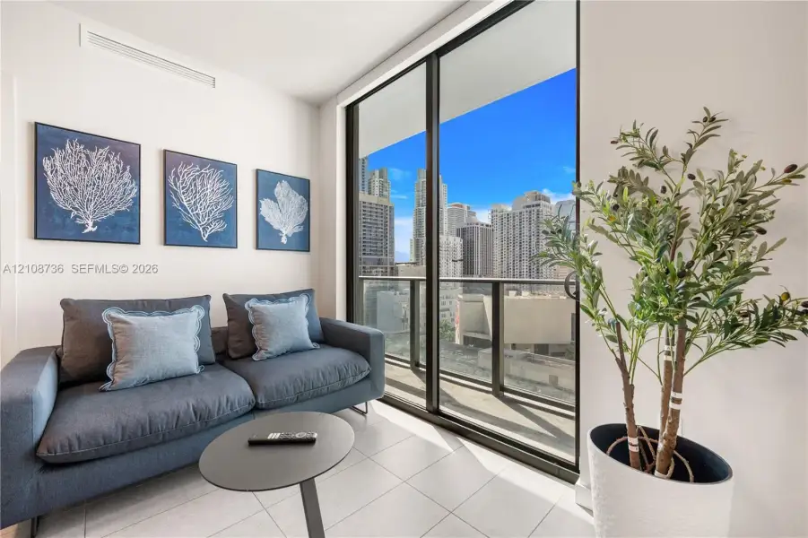 Floor-to-ceiling sliding glass doors, private balcony with metal railing, light-colored tile flooring, and urban skyline backdrop Floor-to-ceiling sliding glass doors, private balcony with metal railing, light-colored tile flooring, and urban skyline backdrop